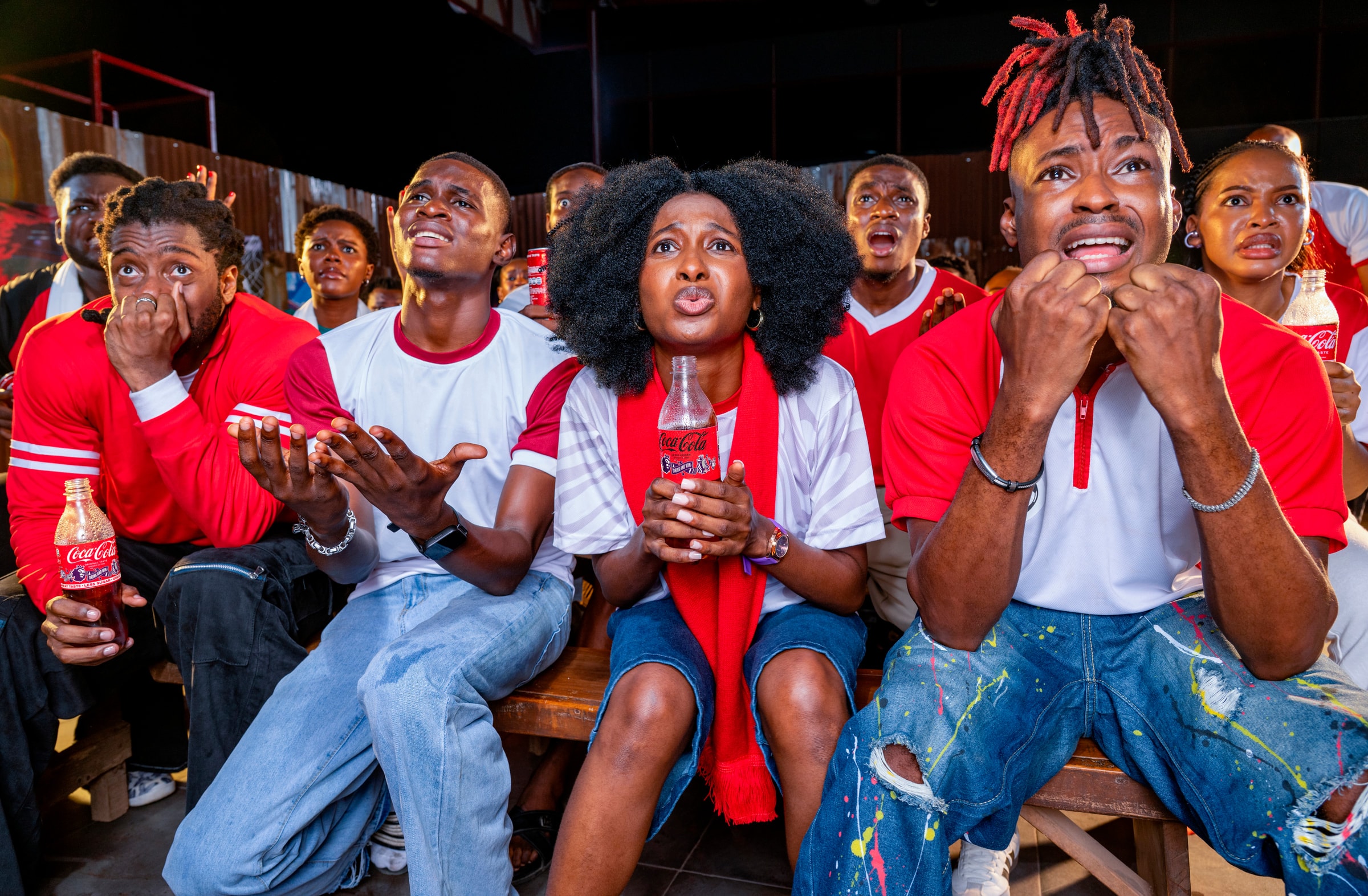 Fans watching a match together, holding bottles of Coca-Cola